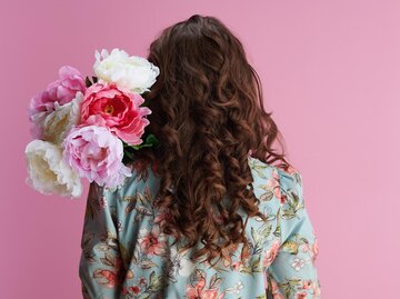 Rückenansicht von Frau mit braunen, voluminösen Haaren, die Pfingstrosen im Arm hält | © Getty Images/CentralITAlliance