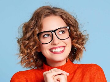 Begeisterte junge Frau lächelnd und träumend mit Bobfrisur und Brille | © Getty Images/evgenyatamanenko