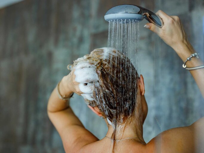 Frau steht in der Dusche und wäscht Shampoo aus ihren Haaren. | © Getty Images/skynesher