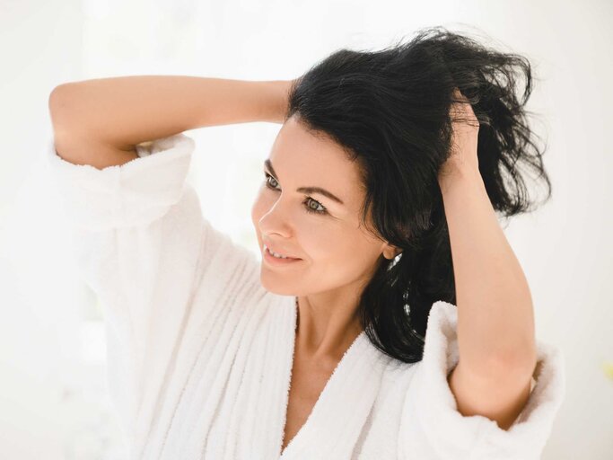 Frau schaut sich ihre Haare im Spiegel an | © Getty Images/Inside Creative House