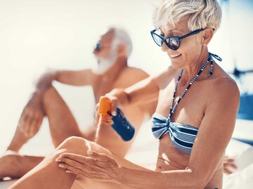 Ältere Frau trägt Sonnencreme auf ihrem Bein auf. | © Getty Images / Aja Koska