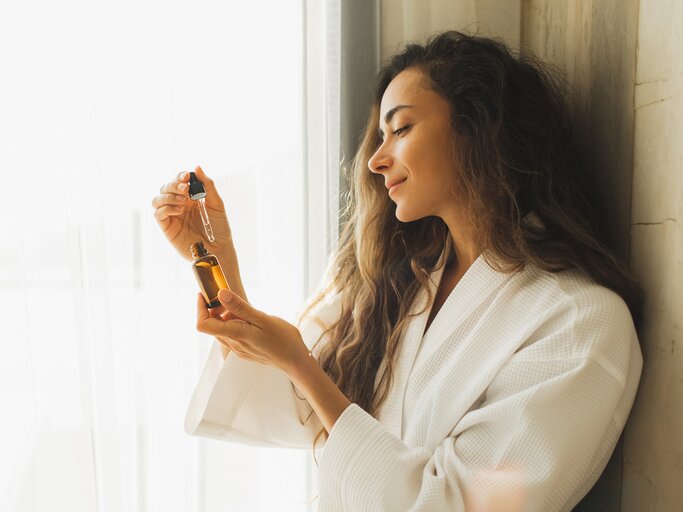 Entspannte Frau im Bademantel mit Serum in der Hand | © GettyImages/Anastasiia Krivenok