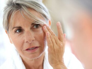 Ältere Frau betrachtet ihre Haut im Spiegel | © Adobe Stock/goodluz