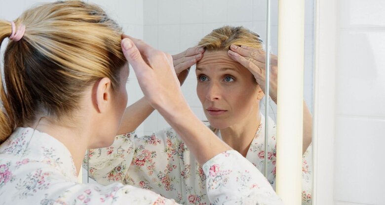 Person sieht sich Stirnfalten im Spiegel an | © Getty Images/Robert Decelis