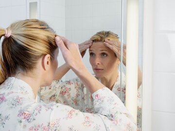 Person sieht sich Stirnfalten im Spiegel an | © Getty Images/Robert Decelis