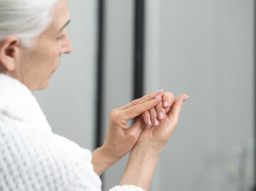 Ältere Frau mit grauen Haaren betrachtet ihre Fingernägel. | © Getty Images / brizmaker