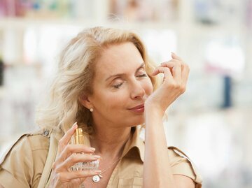 Blonde ältere Frau riecht an ihrem Handgelenk, auf das sie Parfum aufgetragen hat. | © Getty Images / Martin Barraud