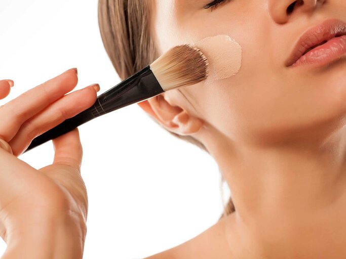 Frau trägt mt einem Pinsel Make-up im Gesicht auf. | © Adobe Stock/vladimirfloyd