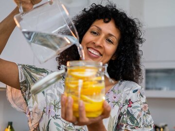 Frau gießt sich Zitronenwasser aus einer Karaffe in ein Glas ein | © Getty Images/D-Keine