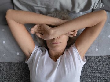 Frau liegt mit verschränkten Armen über dem Gesicht auf dem Bett | © Getty Images/fizkes