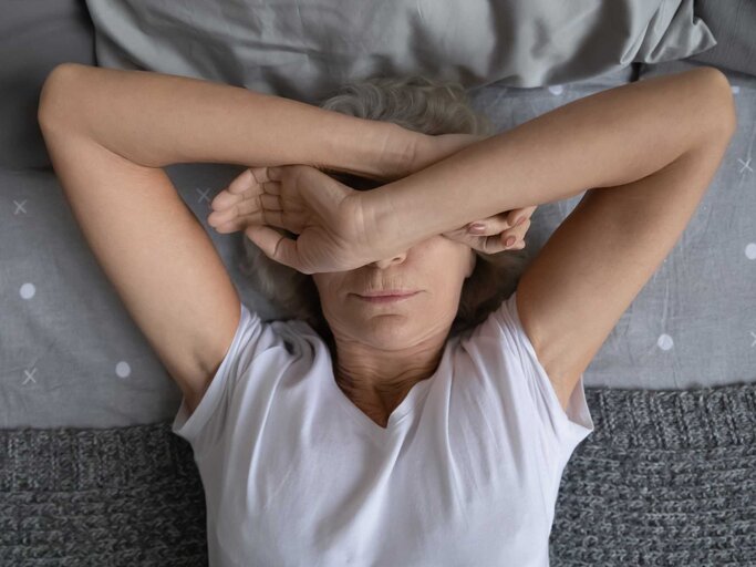 Frau liegt mit verschränkten Armen über dem Gesicht auf dem Bett | © Getty Images/fizkes