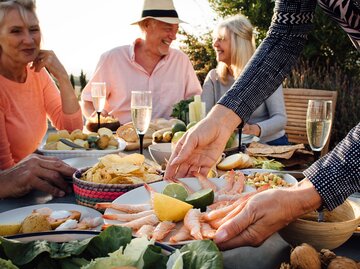 Menschen sitzen am Tisch und essen mediterranes Essen. | © GettyImages/SolStock