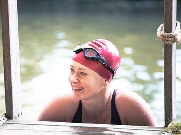 Person mit Schwimmbrille und -kappe steigt aus Badesee | © Getty Images/Gary Yeowell