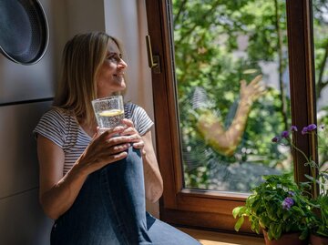Person sitzt mit Wasserglas an Fenster | © Getty Images/Westend61