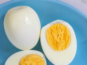 Gekochte Eier liegen aufgeschnitten auf einem blauen Teller. | © Getty Images / Manuel Mocanu