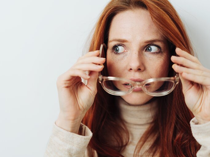 Eine Frau setzt ihre Brille ab und macht dabei große Augen | © GettyImages/stockfour