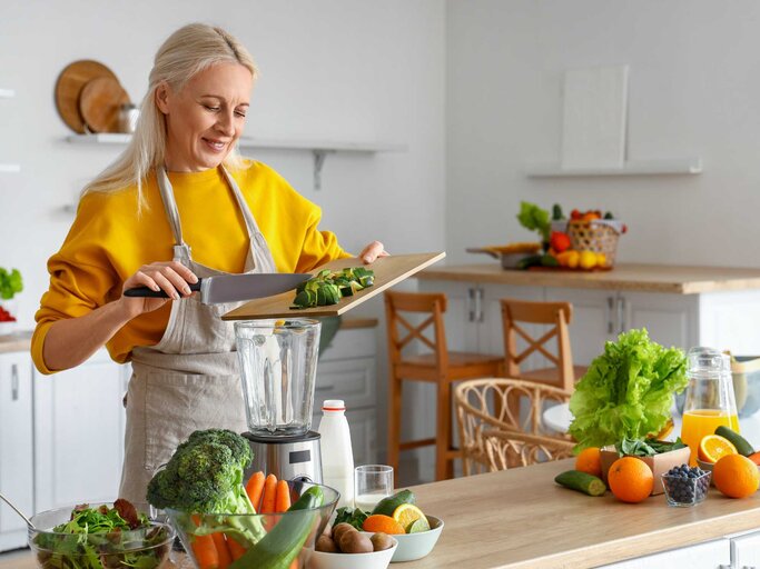 Frau schneidet Gemüse und gibt es in einen Mixer | © Adobe Stock/Pixel-Shot