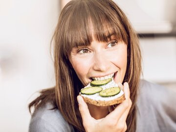 Eine Frau beißt in eine Scheibe Brot mit Frischkäse und Gurke | © Getty Images / Westend61