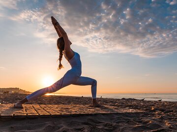 Frau macht in der Morgensonne Yoga am Strand | © AdobeStock/Sergio