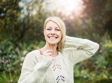 Eine Frau steht im Wald und lächelt glücklich in die Kamera | © Getty Images / Westend61