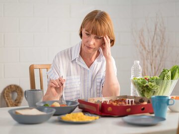 Frau sitzt am Esstisch und hat verschiedene Gericht vor sich stehen. | © Adobe Stock/sutthinon602