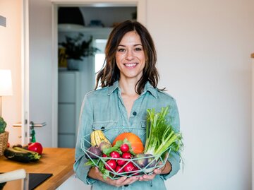 Porträt einer Frau mir einem buntgemischten Obst- und Gemüsekorb in den Händen | © Getty Images / Westend61