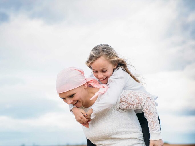 Frau mit Kind auf dem Rücken und rosa Kopftuch | © Adobe Stock/karrastock