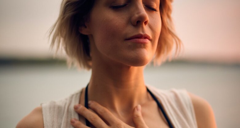 Frau beruhigt sich, indem sie ihre Hand auf die Brust hält und die Augen schließt | © Unsplash/Darius Bashar