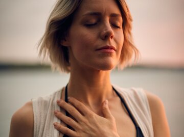 Frau beruhigt sich, indem sie ihre Hand auf die Brust hält und die Augen schließt | © Unsplash/Darius Bashar