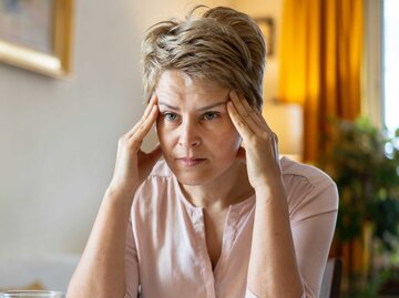 Frau sitzt am Tisch und fasst sich an die Schläfen | © Getty Images/Vladimir Vladimirov