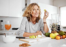 Ältere Frau steht in der Küche und isst einen Apfel