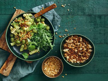 Sommerlicher vegetarischer Nudelsalat mit Brokkolipesto, Erbsen, Rucola, Oliven, Pinienkernen und Semmelbröseln auf dunkelgrünem Hintergrund. Draufsicht. | © Getty Images/luchezar