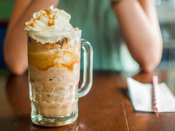 Ein großes Glas mit Frappucino (Eiskaffee mit Karamellsirup und Sohne) auf einem Holztisch | © Getty Images/Karl Tapales