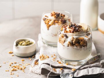 Zwei Gläser mit griechischem Joghurt, Nüssen und Müsli auf einem Holztisch  | © Getty Images/Roxiller