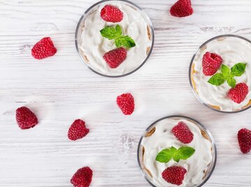 Gläser mit Cheesecake-Trifle gefüllt und mit frischen Himbeeren garniert auf einem Tisch, Aufnahme von oben | © Getty Images/from_my_point_of_view