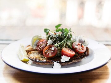 Kirschtomaten und zerdrückte Avocado-Bruschetta, serviert auf geröstetem Sauerteigbrot auf einem Holztisch - Stockfoto | © Getty Images/Naomi Rahim