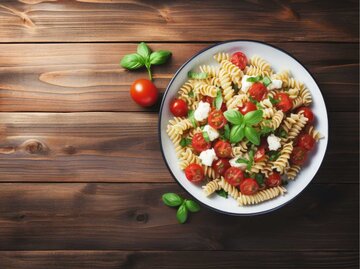 Nudelsalat mit Makkaroni, Feta-Käse und Tomaten auf Holztisch. | © Adobe Stock/chandlervid85