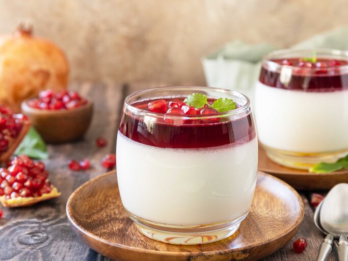 Panna Cotta mit Granatapfel-Gelee und Minze auf einem hölzernen Hintergrund. | © Adobe Stock/elena_hramowa