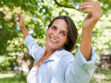 Reife Frau tanzt und lächelt in der Natur | © Getty Images/Westend61