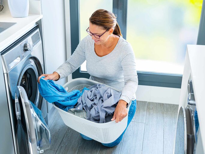 Frau, die die Waschmaschine mit Wäsche belädt | © Getty Images/fcafotodigital