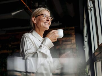 Lächelnde Person mit Kaffeetasse in der Hand | © Getty Images/Westend61