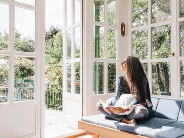 Eine Frau hat ein Buch in der Hand und schaut aus dem Fenster | © GettyImages/Westend61