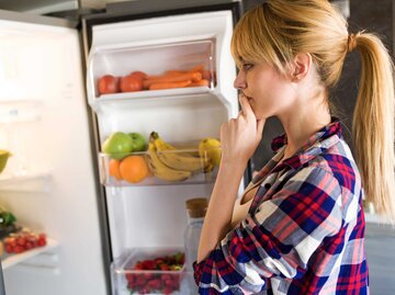 Frau steht vor einem geöffneten Kühlschrank. | © Getty Images / nensuria