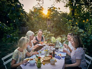 Freundinnen sitzen bei Sonnenuntergang um einen Tisch im Garten | © Getty Images/Uwe Krejci