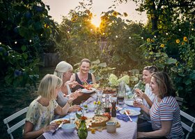 Freundinnen sitzen bei Sonnenuntergang um einen Tisch im Garten