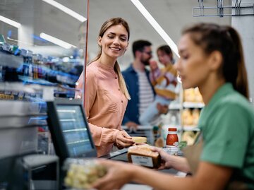 Frau, die Lebensmittel an die Kasse im Supermarkt stellt | © Getty Images/Drazen Zigic