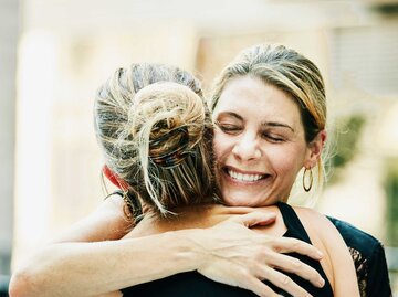 Lachende, blonde Frau umarmt blonde Frau mit Dutt | © Getty Images/Thomas Barwick