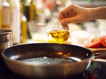 Hand gießt Olivenöl in eine Pfanne | © Getty Images/Igor Ploskin