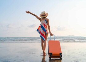 Glückliche Frau in Urlaubsstimmung mit Rollkoffer am Strand