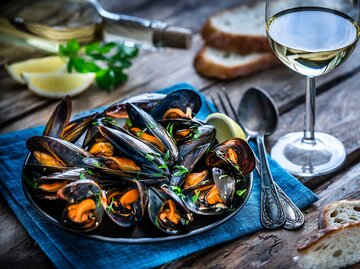 Ein Teller mit Miesmuscheln steht neben einem Glas Weißwein auf dem Tisch. | © Getty Images / fcafotodigital